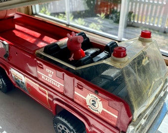 Puede incluir: Un camión de bomberos de juguete rojo con el texto "City of Blazedale" y "Fire 2 Rescue". Una figura de cerdo rosa está en el asiento del conductor. El camión tiene una escalera blanca y neumáticos negros.