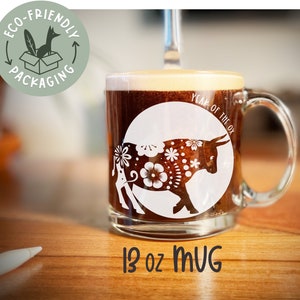May include: A white ceramic mug with a black and white illustration of an ox with floral designs. The mug says "Year of the Ox" and is 13 oz.