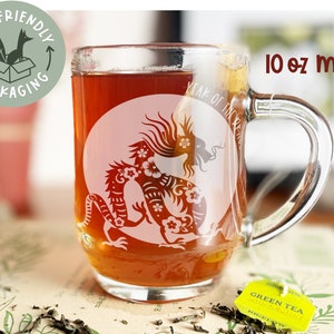 May include: A clear glass 10 oz mug with a white design of a dragon with flowers. The mug is filled with a dark brown liquid. The text "Year of the Dragon" is visible on the mug.