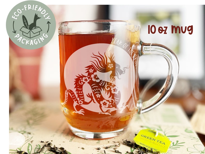 May include: A clear glass 10 oz mug with a white design of a dragon with flowers. The mug is filled with a dark brown liquid. The text "Year of the Dragon" is visible on the mug.