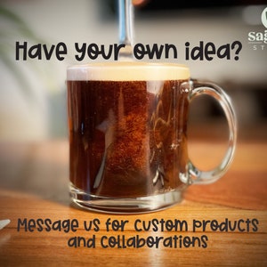 May include: A glass mug filled with coffee, with a caption that reads "Have your own idea?" and "Message us for custom products and collaborations". The mug is sitting on a wooden surface.