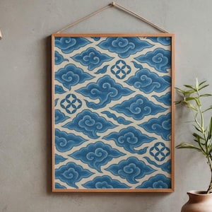 Op de afbeelding: Een ingelijste print met een herhalend patroon van gestileerde blauwe wolken op een crèmekleurige achtergrond. Het kunstwerk wordt gepresenteerd in een lichtbruine houten lijst en hangt aan een natuurlijk touw. Een decoratief wandkunstwerk.