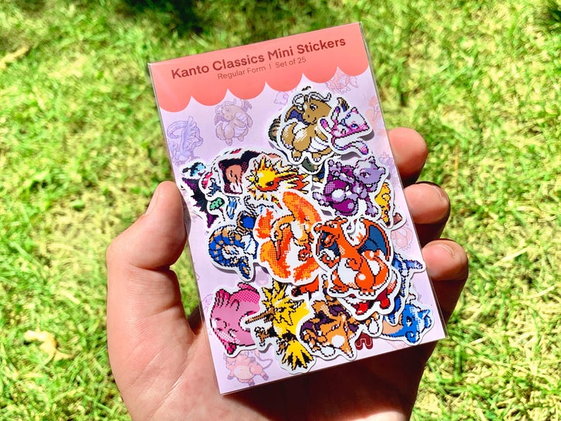 Pu&ograve; includere: Un pacchetto di mini adesivi Kanto Classics, Forma regolare 1, Set di 25, con vari personaggi dei cartoni animati colorati. Gli adesivi sono esposti su uno sfondo rosa, su uno sfondo di erba verde.