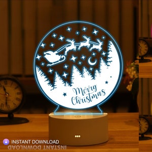 May include: A white 3D printed night light with a design of Santa Claus in a sleigh pulled by reindeer flying through a snowy forest with stars and a crescent moon. The text "Merry Christmas" is written below the design. The night light is illuminated in blue, pink, and yellow.