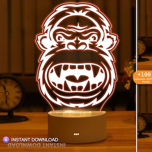 Może przedstawiać: Lampka nocna drukowana w 3D w kształcie wściekłego goryla z białym obrysem. Lampka stoi na białej podstawie z trzema małymi czarnymi kropkami. Obraz pokazuje trzy różne opcje kolorystyczne lampki: pomarańczowy, zielony i niebieski. Tekst "+100 Dostosuj różne wzory" jest widoczny na obrazie.
