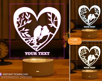 May include: White night light with a heart-shaped design featuring two birds perched on a branch. The heart is cut out and the light shines through the design. The base of the light is white and has a button on the side. The text "YOUR TEXT" is displayed on the light.