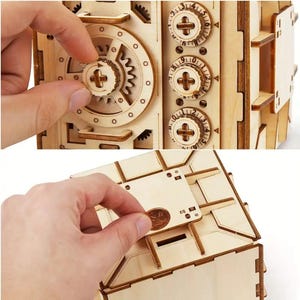 May include: A wooden model of a safe with three dials and a slot for inserting a coin. The safe is open and the inside is visible. The safe is made of light brown wood and has a realistic design.