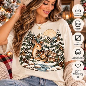 Puede incluir: Una camiseta de color crema con un estampado gráfico de dos ciervos descansando en un paisaje forestal nevado con montañas, un sol, pinos y piñas. Los ciervos y partes de los árboles tienen estampados de leopardo y cuadros.
