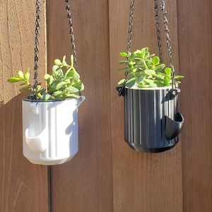 May include: Two hanging planters with black chains, one white and one black, each with a succulent plant inside.