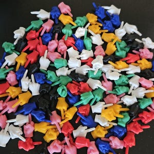 May include: A large collection of small, plastic hand figurines in various colors including red, blue, yellow, green, white, pink, and black. Each figurine is shaped into a hand gesture with the middle finger extended in an upright position.