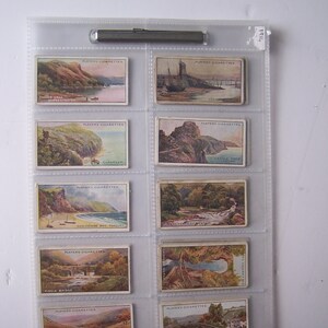 May include: A collection of 10 vintage cigarette cards featuring scenic views of the British Isles. The cards are in a clear plastic album with a metal clip. The cards feature images of Falcon Crag, Clovelly, Castle Rock, Godicombe Bay, Waterwheel, Fingle Bridge, The Soane Valley, and The Iron Bridge.