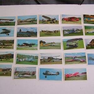 May include: A collection of 20 vintage trading cards featuring different types of airplanes. The cards are arranged in four rows of five cards each. Each card features a colorful illustration of a different airplane, with some cards showing the airplane in flight and others showing it on the ground.