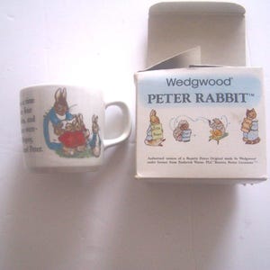 May include: A white ceramic mug featuring a colorful illustration of Peter Rabbit and text from the story, accompanied by its original cardboard box. The box displays the Wedgwood Peter Rabbit logo, additional character illustrations, and text.