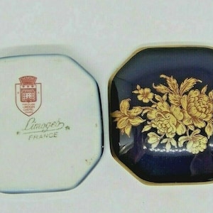 以下が含まれることがあります： フランスの Limoges 製の磁器製の小物入れで、青と金の色の花柄が施されています。蓋には、"Porcelaine Limoges Castel France" と書かれた紋章があります。