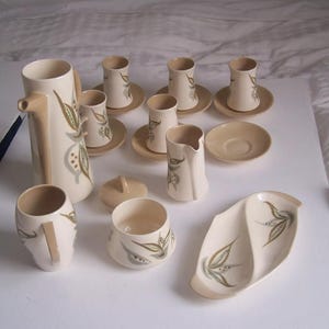 May include: A set of cream-coloured ceramic teacups and saucers with a floral design. The set includes a teapot, creamer, sugar bowl, and a serving tray.