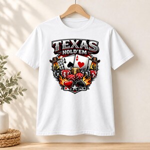 May include: A white short-sleeve t-shirt featuring a graphic print of Texas Hold'em poker elements, including playing cards, stacks of casino chips, red dice, and flames, with the text "TEXAS HOLD'EM" displayed in bold lettering at the top.