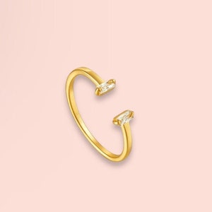 May include: A gold ring with two clear baguette-shaped stones set on the band.