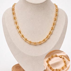 May include: A gold-toned necklace featuring a series of elongated U-shaped links connected by small spheres, accompanied by a matching gold-toned bracelet with a lobster claw clasp and an adjustable chain extension, displayed as a set.