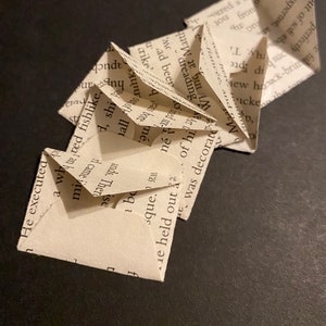 May include: A handmade paper sculpture made from book pages. The folded paper is arranged in a zig-zag pattern, with visible text from the book. The sculpture is set against a dark background, highlighting the off-white color of the paper.