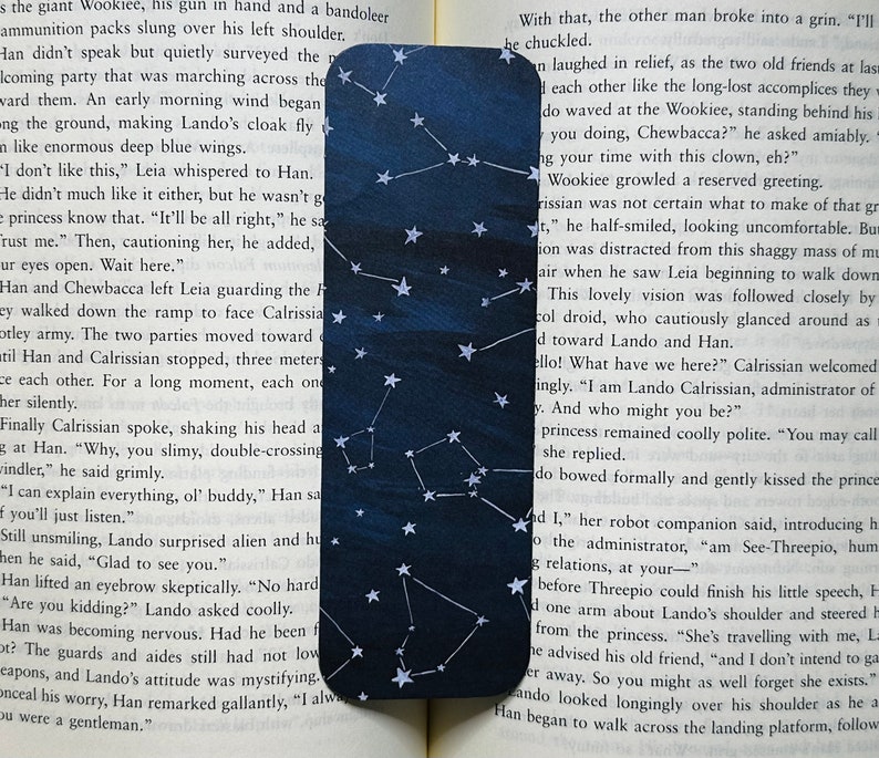 A bookmark is laid out on the pages of an open book. It has a dark blue varied background with white stars and constellations.