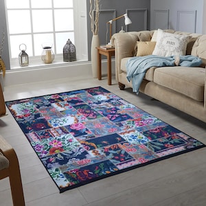 May include: A colourful patchwork rug with floral patterns on a navy blue background. The rug is in a living room setting with a sofa and a side table.