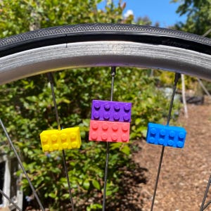 May include: A bicycle wheel with colorful, brick-shaped accessories attached to the spokes. The accessories are yellow, pink, purple, and blue. The tire is black, and the wheel is silver.