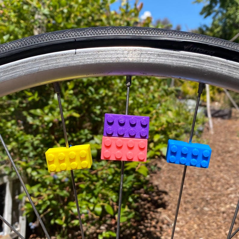 May include: A bicycle wheel with colorful, brick-shaped accessories attached to the spokes. The accessories are yellow, pink, purple, and blue. The tire is black, and the wheel is silver.