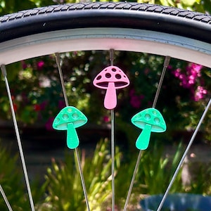 Puede incluir: Tres cuentas para radios con forma de seta fijadas a los radios de una rueda de bicicleta. Una cuenta rosa est&aacute; situada en la parte superior, mientras que dos cuentas de color verde brillante se encuentran a cada lado debajo de ella.