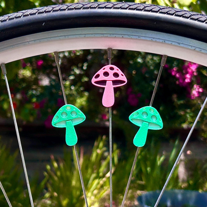 Puede incluir: Tres cuentas para radios con forma de seta fijadas a los radios de una rueda de bicicleta. Una cuenta rosa est&aacute; situada en la parte superior, mientras que dos cuentas de color verde brillante se encuentran a cada lado debajo de ella.