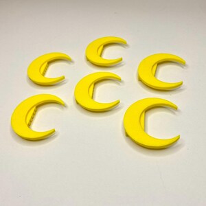 May include: Six bright yellow crescent moon-shaped objects. Each moon has a curved design with a straight edge on the inside. The objects are evenly spaced against a white background. The moons are likely decorative or craft elements.