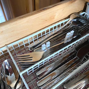 Puede incluir: Un cajón de cocina abierto que contiene cubiertos de acero inoxidable, incluyendo tenedores, cuchillos y cucharas, ordenados en un compartimento de plástico blanco. El cajón es de madera clara.