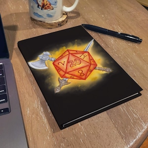 May include: A black notebook with a red 20-sided die and two swords crossed behind it. The die is glowing with a yellow and orange light. The notebook has a black cover and a white border.