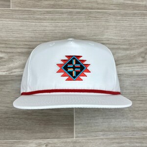 Könnte beinhalten: Weiße Baseballkappe mit roter Kordel und einem bunten, gestickten geometrischen Muster auf der Vorderseite.