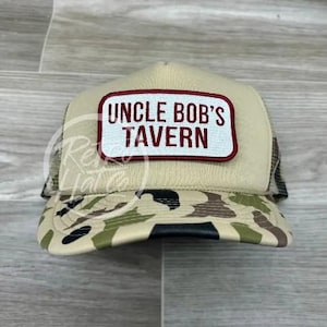 May include: A beige and camouflage trucker hat with a red and white patch that says "Uncle Bob's Tavern".
