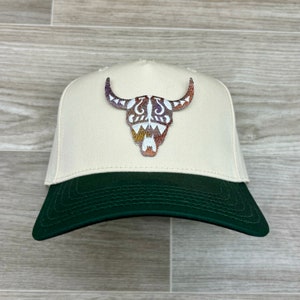 May include: A beige and green baseball cap with a colorful embroidered bull skull design on the front.