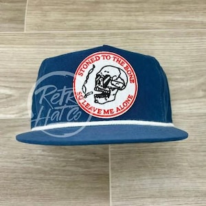 Könnte beinhalten: Eine blaue und weiße Baseballkappe mit einem weißen gestickten Aufnäher, auf dem "Stoned to the Bone So Leave Me Alone" mit einem Totenkopf- und Knochenmotiv steht.