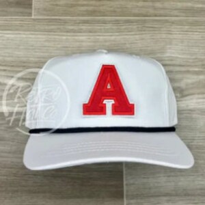 May include: White baseball cap with a red felt letter 'A' on the front. The cap has a black rope strap.