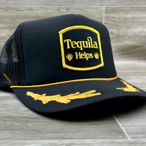May include: Black trucker hat with a yellow embroidered patch that says "Tequila Helps" with agave plants on either side of the word "Helps".