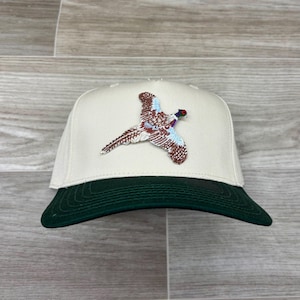 Puede incluir: Una gorra de béisbol blanca con una visera verde y un diseño de faisán bordado.