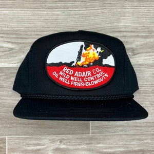 May include: Black trucker hat with a red, white, and yellow patch that reads "Red Adair Co. Wild Well Control Oil Well Fires-Blowouts".