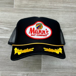 May include: Black trucker hat with a gold trim and a red, white and blue embroidered patch that says "Mann's Bait Company" with an image of an American Indian chief.