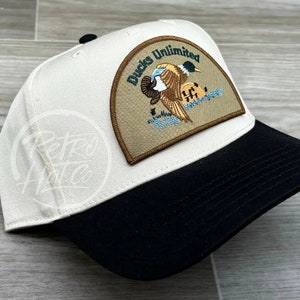 May include: A white and black baseball cap with a brown patch featuring a duck and the text "Ducks Unlimited".