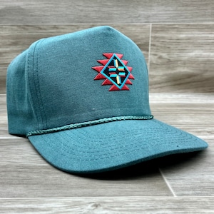 May include: A teal blue trucker hat with a colorful geometric design embroidered on the front. The hat has a mesh back and a rope strap.