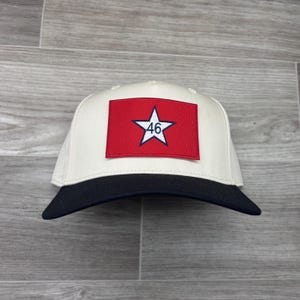May include: A baseball cap with a cream crown and a black peak. The front displays a red rectangle with a white star and the number 46. This hat is a classic, casual accessory.