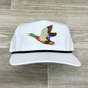 Puede incluir: Gorra de béisbol blanca con visera negra y una imagen bordada de un pato silvestre en vuelo.