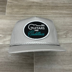 May include: A gray trucker hat with a black and white patch that says "Guitars and Cadillacs" in white text with a teal blue outline.