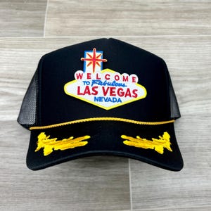 May include: Black trucker hat with a yellow and gold embroidered design. The hat features a patch with the text "Welcome to Fabulous Las Vegas Nevada".