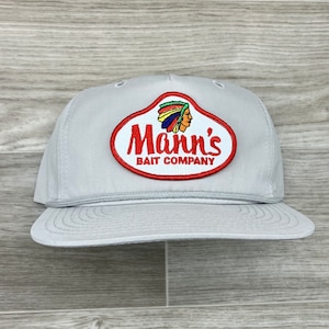 May include: Gray baseball cap with a red, white, and blue patch that says "Mann's Bait Company" with an illustration of a Native American wearing a headdress.