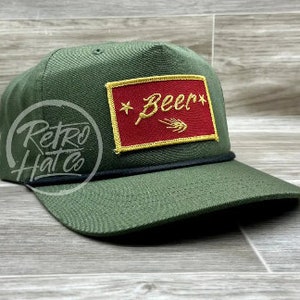 May include: A green trucker hat with a black brim and a red and gold patch that says "*Beer*" with a wheat stalk design.