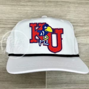 Puede incluir: Gorra de béisbol blanca con una banda de cuerda negra y un parche bordado en rojo, azul y amarillo que dice "KU" con una mascota de pájaro.